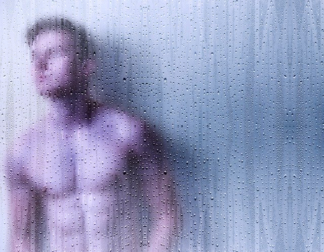 a young man behind a wet glass-curtain in a bathroom